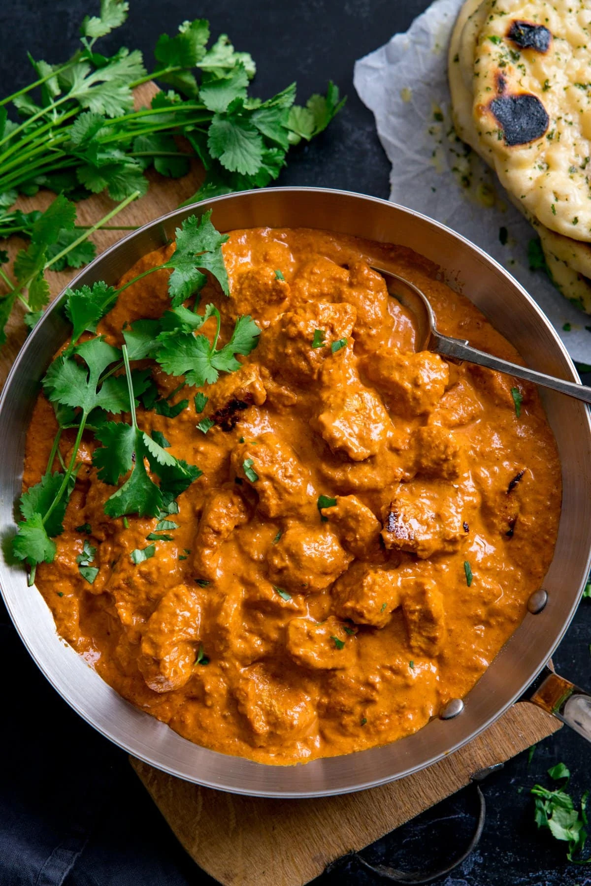 Overhead image of a pan filled with butter chicken curry, topped with fresh coriander. Naan bread just in shot.