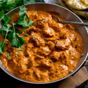 Wide image of Butter Chicken curry in a pan on a dark background.