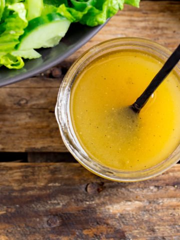 Honey Mustard Salad Dressing in a jar on a wooden table. Part of a bowl of salad just in shot.
