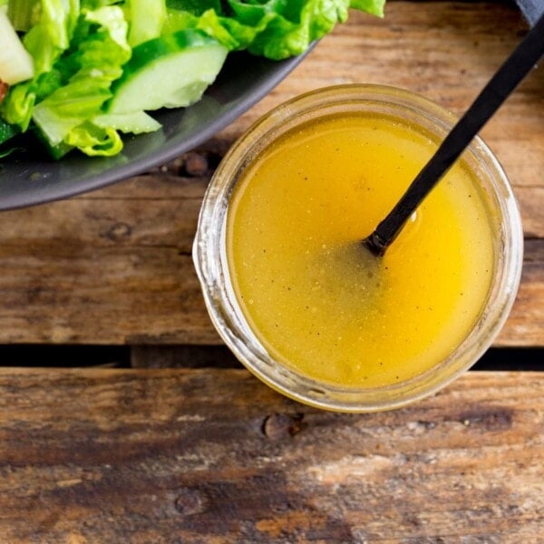 Honey Mustard Salad Dressing in a jar on a wooden table. Part of a bowl of salad just in shot.