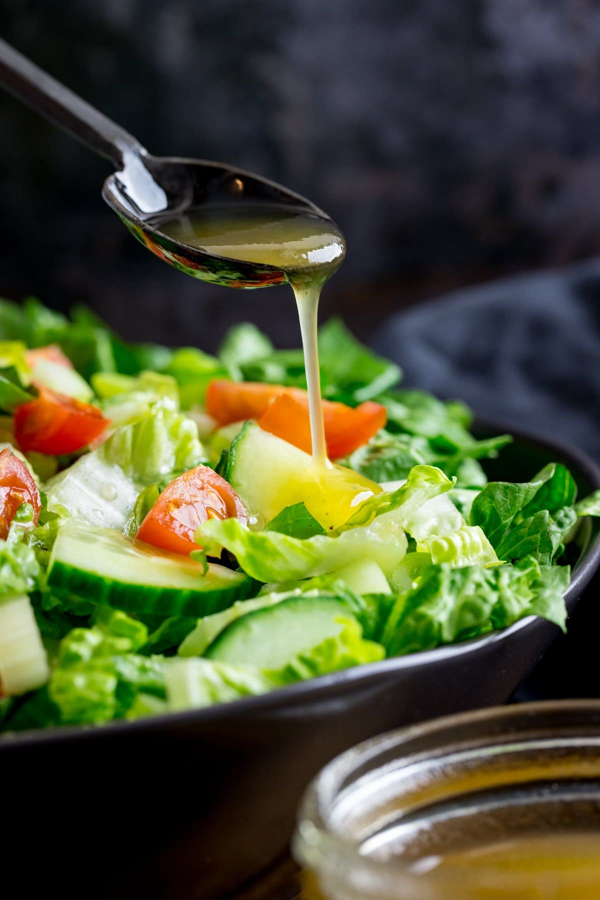 honey mustard salad dressing being poured off a black spoon onto a bowl of salad.