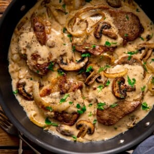Pork steaks in a creamy mushroom sauce in a frying pan.