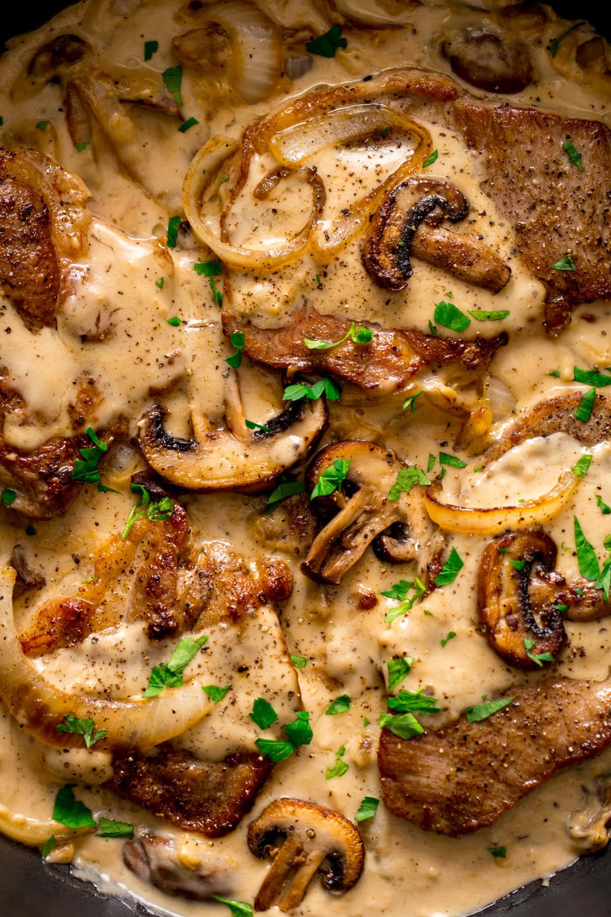 Overhead of pork steak in a cream sauce with mushrooms and onions.