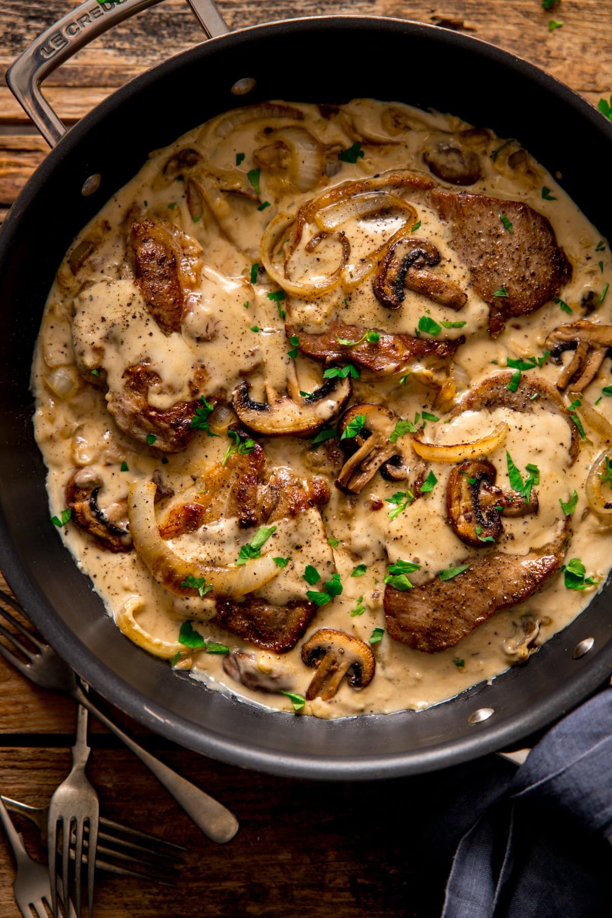 Pork steaks in cream and mushroom sauce in a dark frying pan.