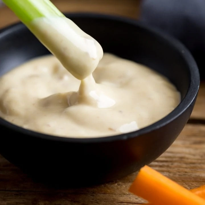 Small black bowl of salad cream with a piece of celery being dipped into it.