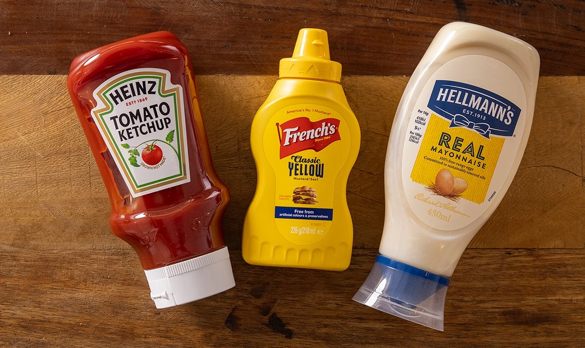 Bottles of ketchup, mayo and mustard on a wooden surface.