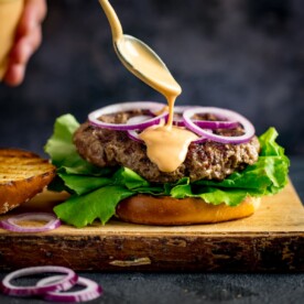Burger sauce being drizzled from a spoon onto an open burger