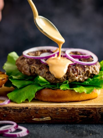 Burger sauce being drizzled from a spoon onto an open burger