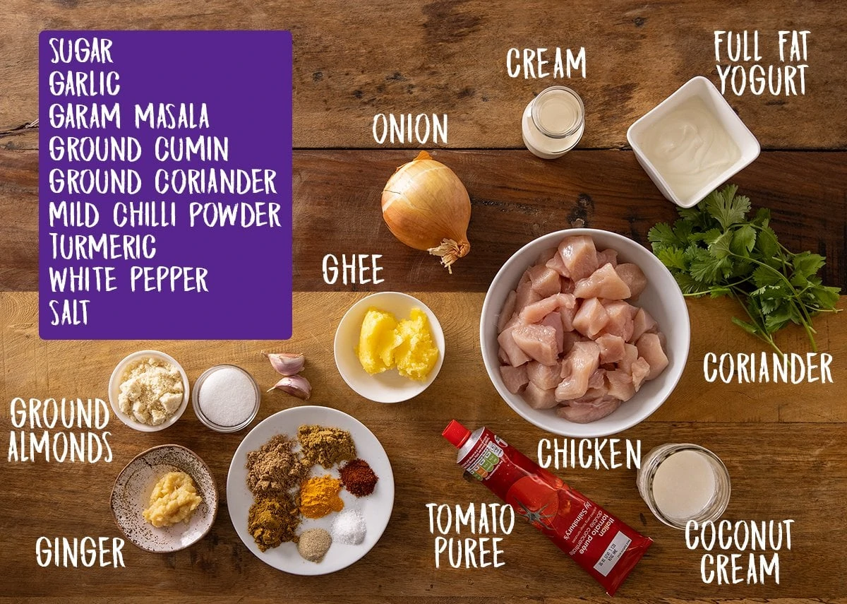 Ingredients for chicken korma on a wooden table.