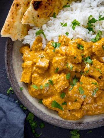 Chicken korma, naan and rice in a bowl on a dark background.