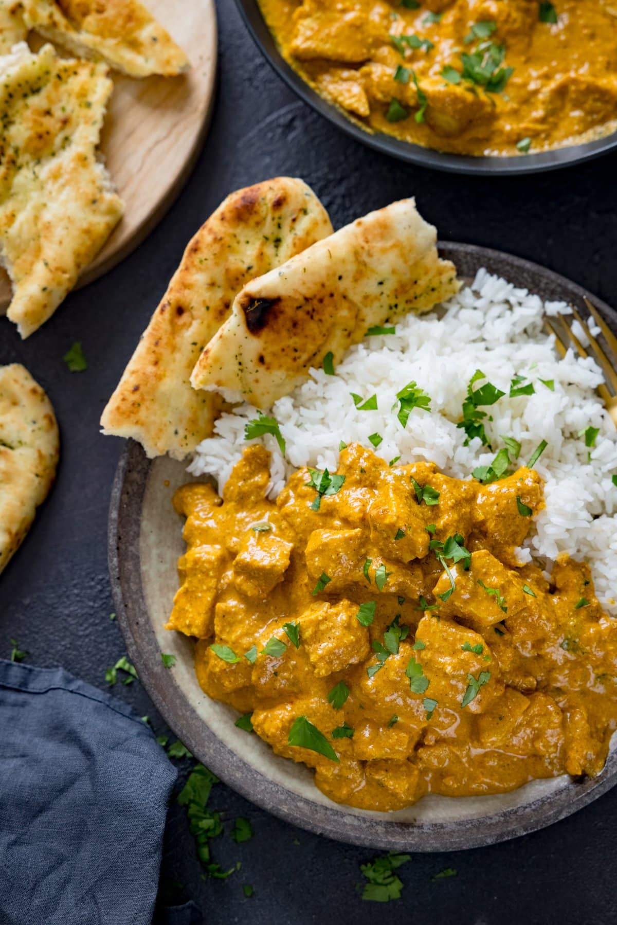 Chicken korma, rice and naan in a bowl on a dark background. Further bowl of curry and naan in background.