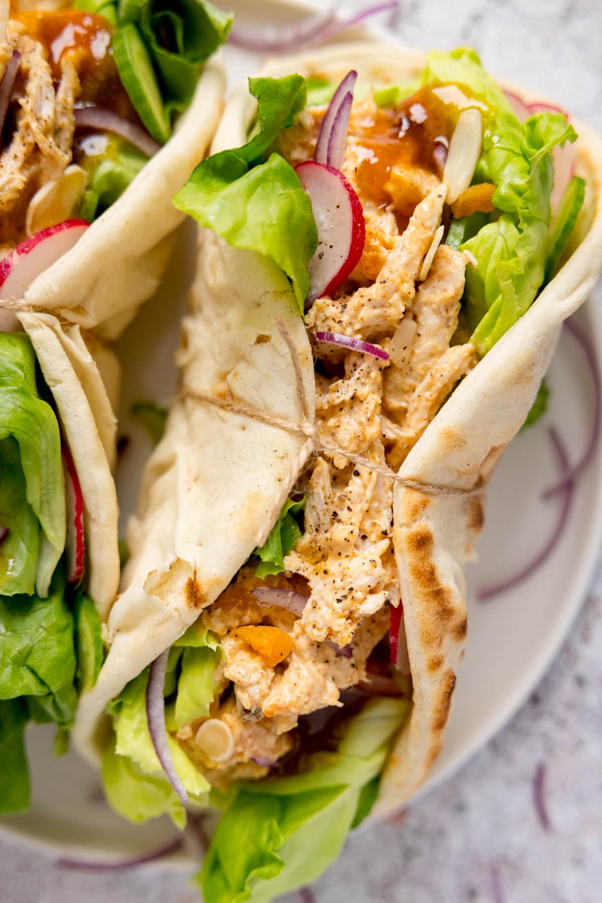 Coronation chicken and salad in a wrap with a piece of string around it. The wrap is on a light plate, next to a further wrap, on a light background.
