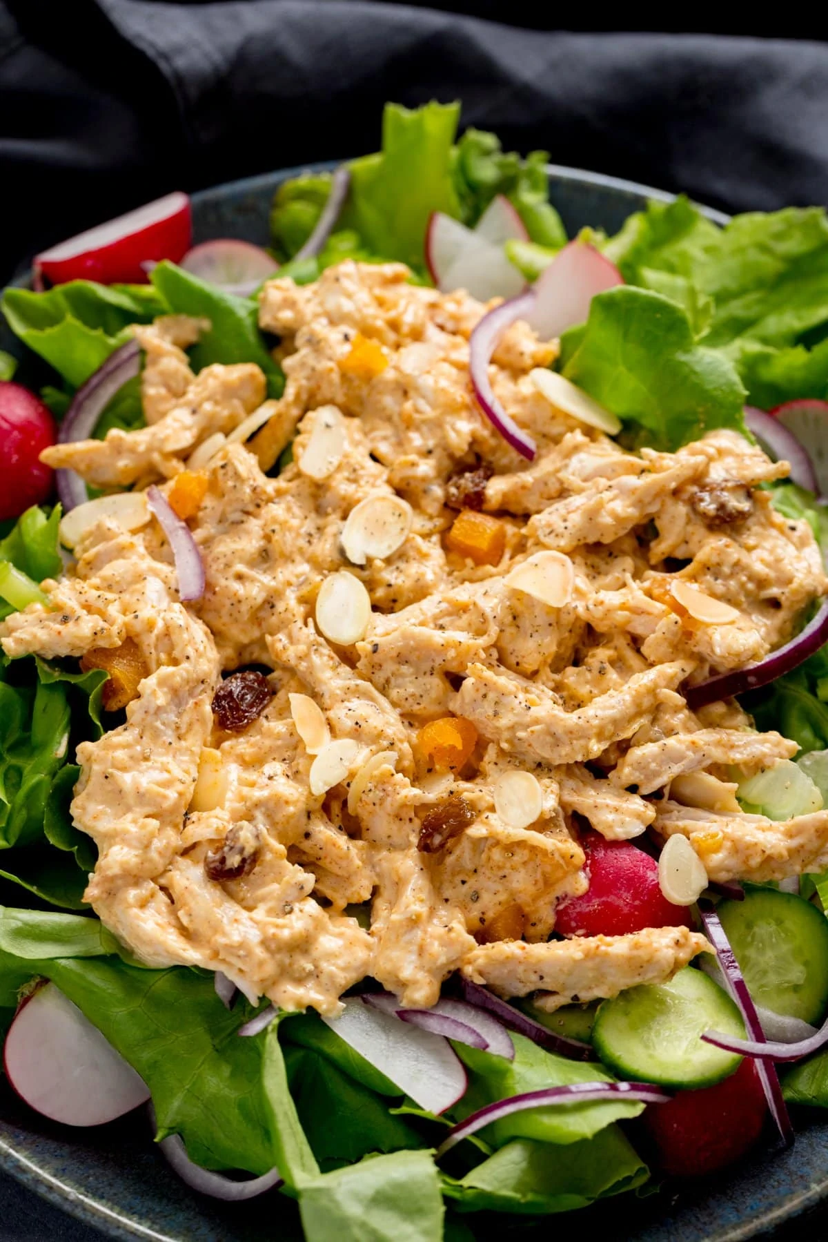 Overhead of coronation chicken on a bed of salad on a dark surface.