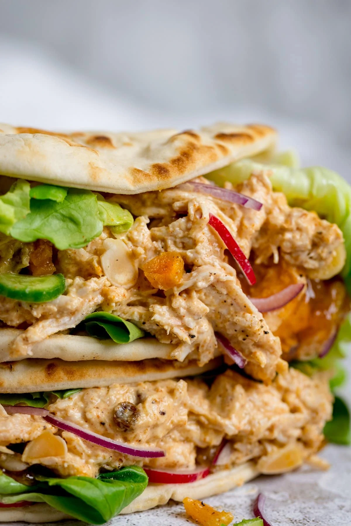 Close up image of coronation chicken and salad on a folded flatbread, stacked on another flatbread, against a light background.
