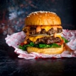 Double cheeseburger on sesame seed bun on a piece of parchment paper on a dark background