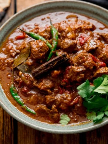 Lamb Bhuna curry in a green bowl on a wooden table