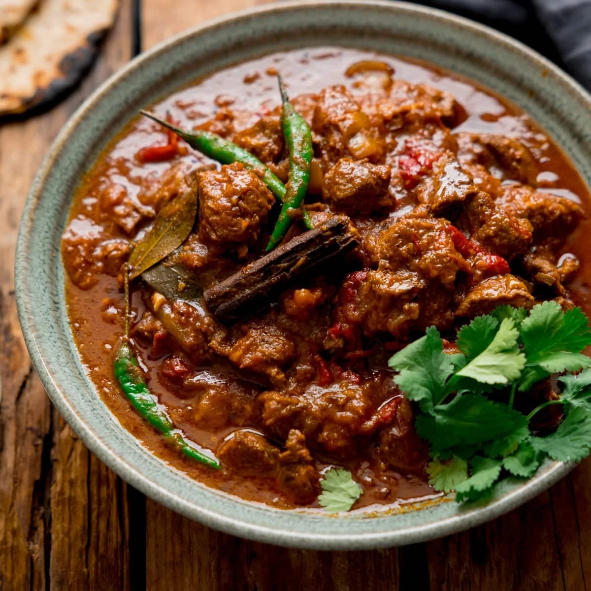 Lamb Bhuna curry in a green bowl on a wooden table