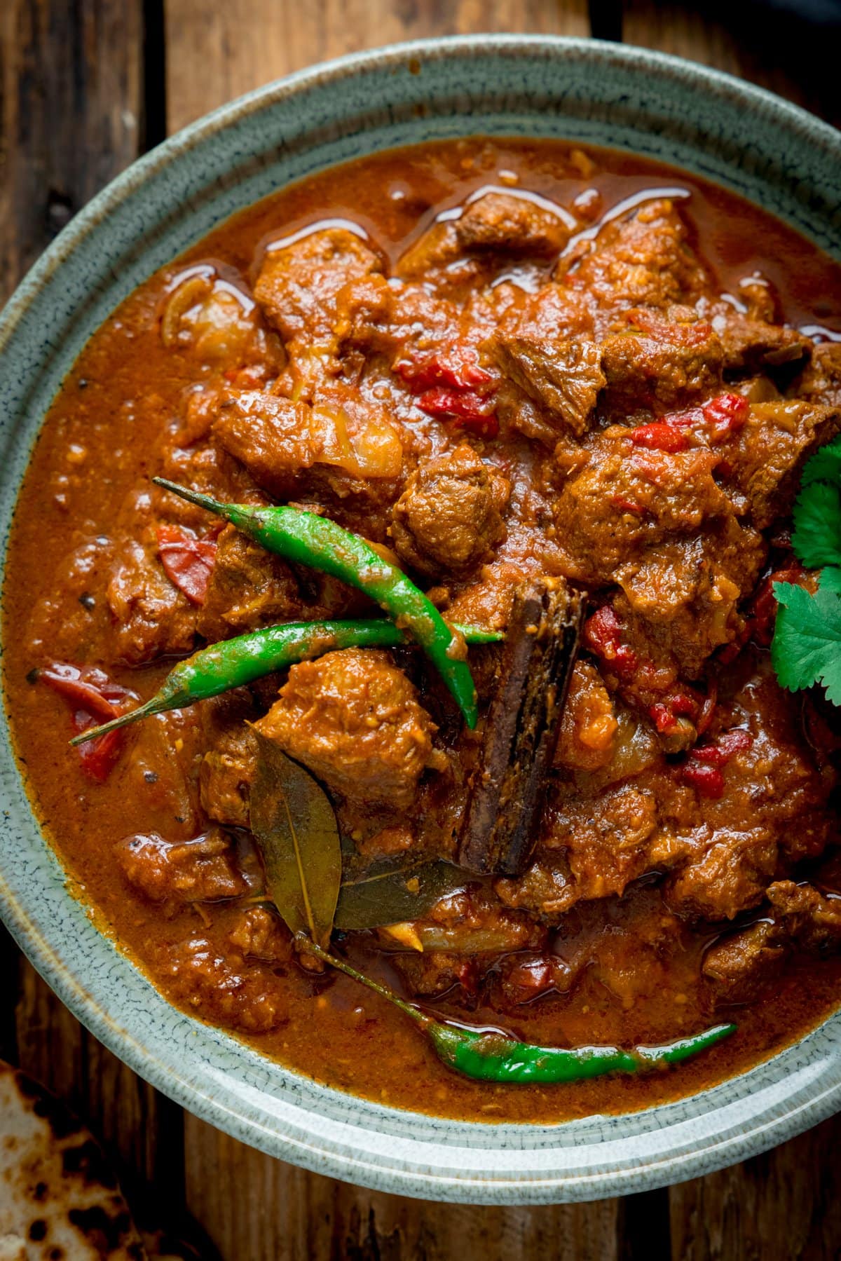 Close up up overhead shot of lamb bhuna curry in a green bowl on a wooden table