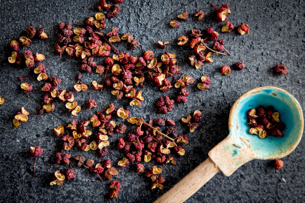 Szechuan peppers scattered on a grey background with a little blue spoon in shot with a wooden handle