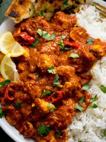 chicken pathia and boiled rice on a white plate. Curry is topped with lemon slices and coriander.