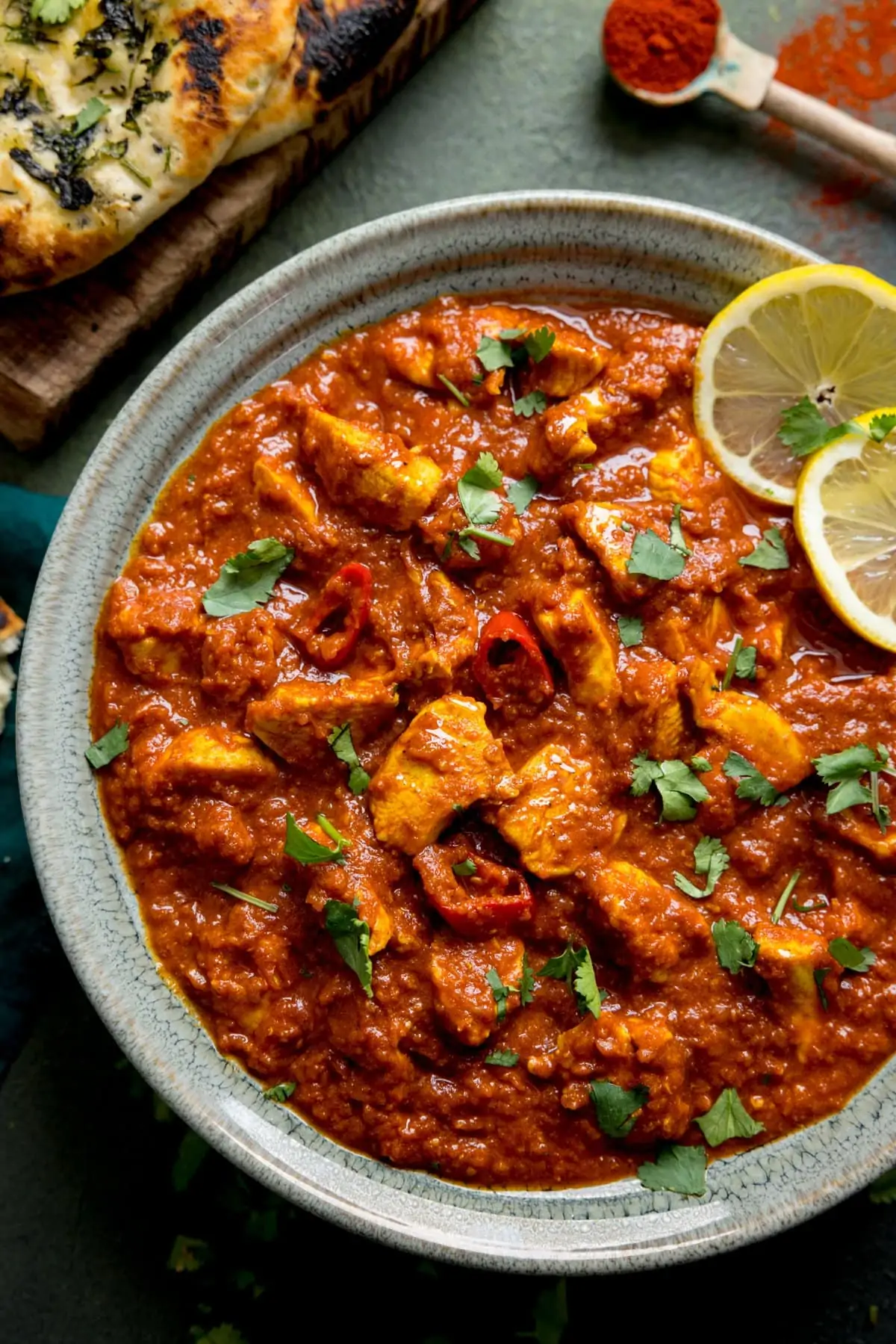 Green bowl filled with chicken pathia curry and topped with lemon slices and coriander.