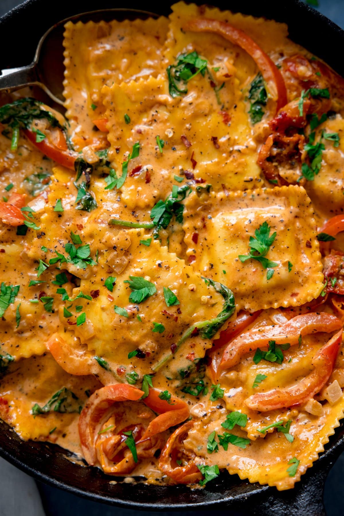 Close up overhead shot of ravioli in cream tomato sauce in a dark pan.