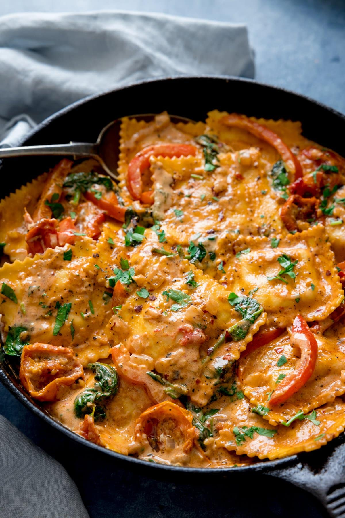 Creamy tomato ravioli in a dark pan on a light background with a light blue napkin next to the pan.