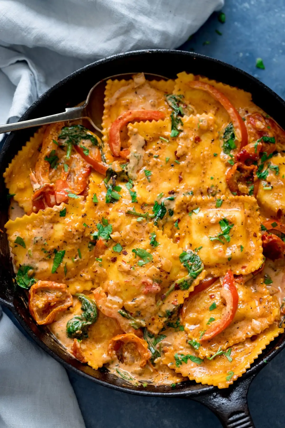 Black pan filled with ravioli in creamy tomato sauce on a blue background.