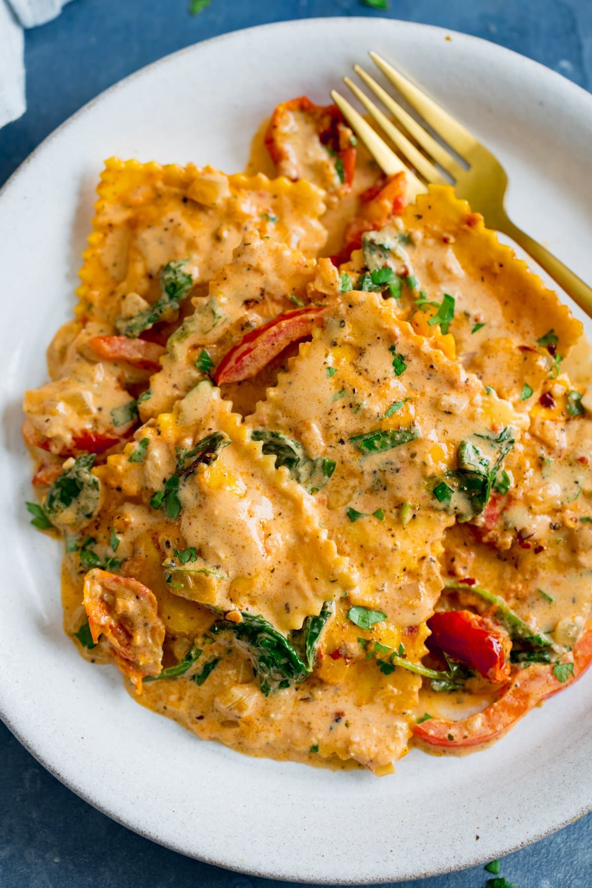 Ravioli in creamy tomato sauce on a white plate with a gold fork, on a blue background.