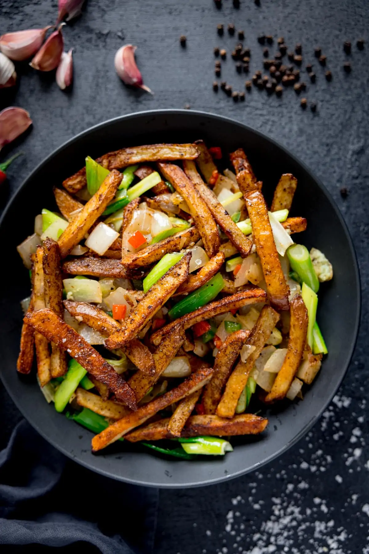 Salt and Pepper Chips in a black bowl on a dark surface. Ingredients scattered around the bowl.