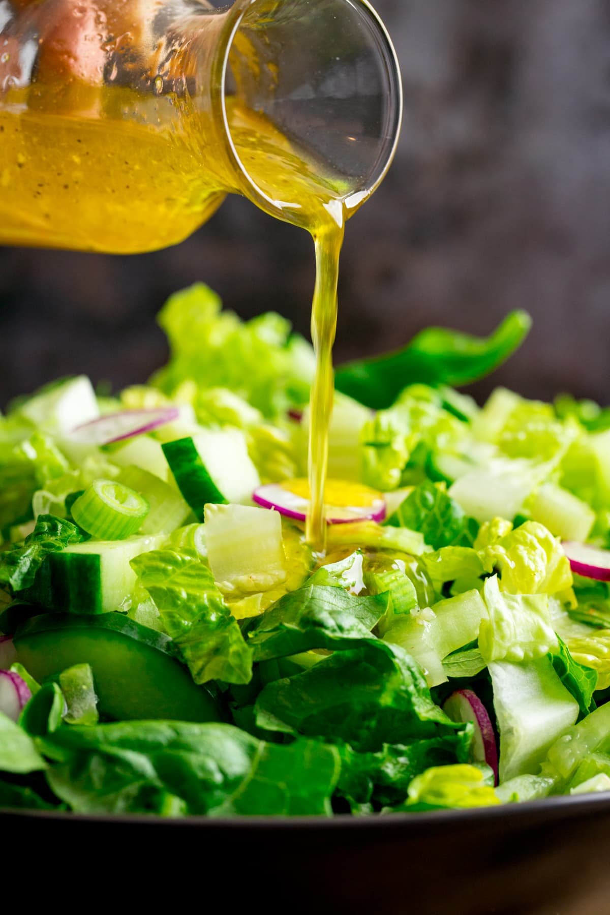 Vinaigrette dressing being poured from a small glass jar onto a green salad.