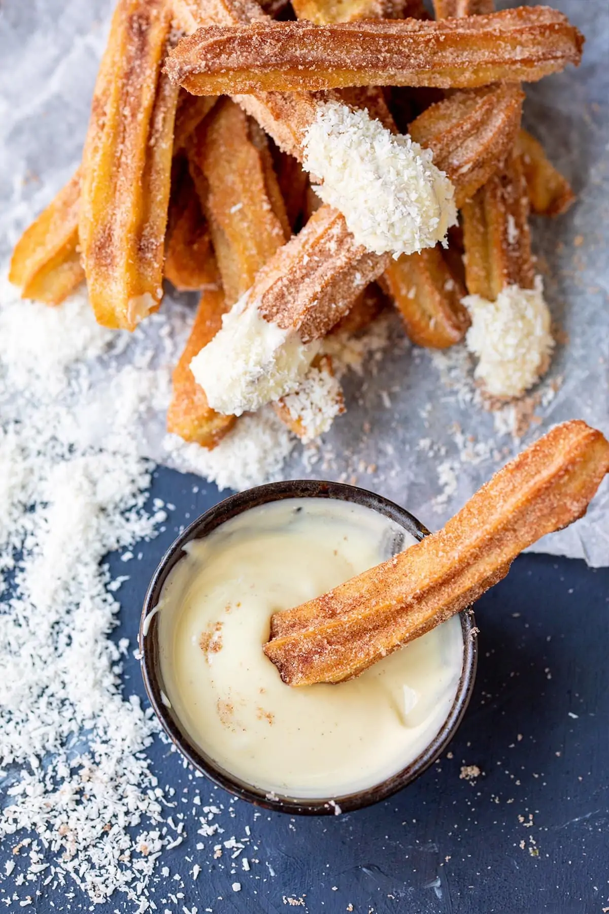 Overhead picture of a churro being dipped into a bowl of melted white chocolate.