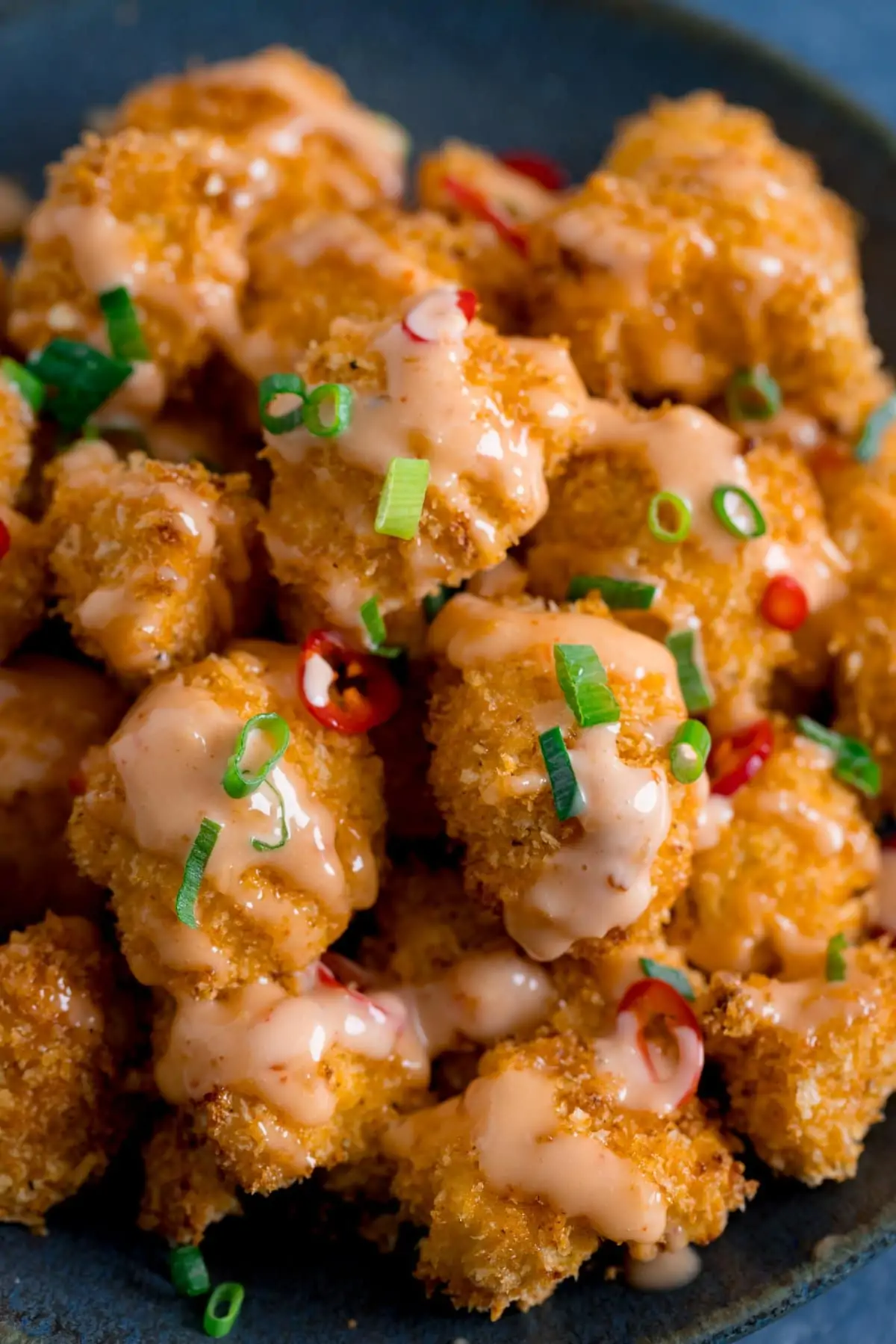 Close up of Crispy Cauliflower with bang bang sauce on a dark plate, topped with chillies and spring onions