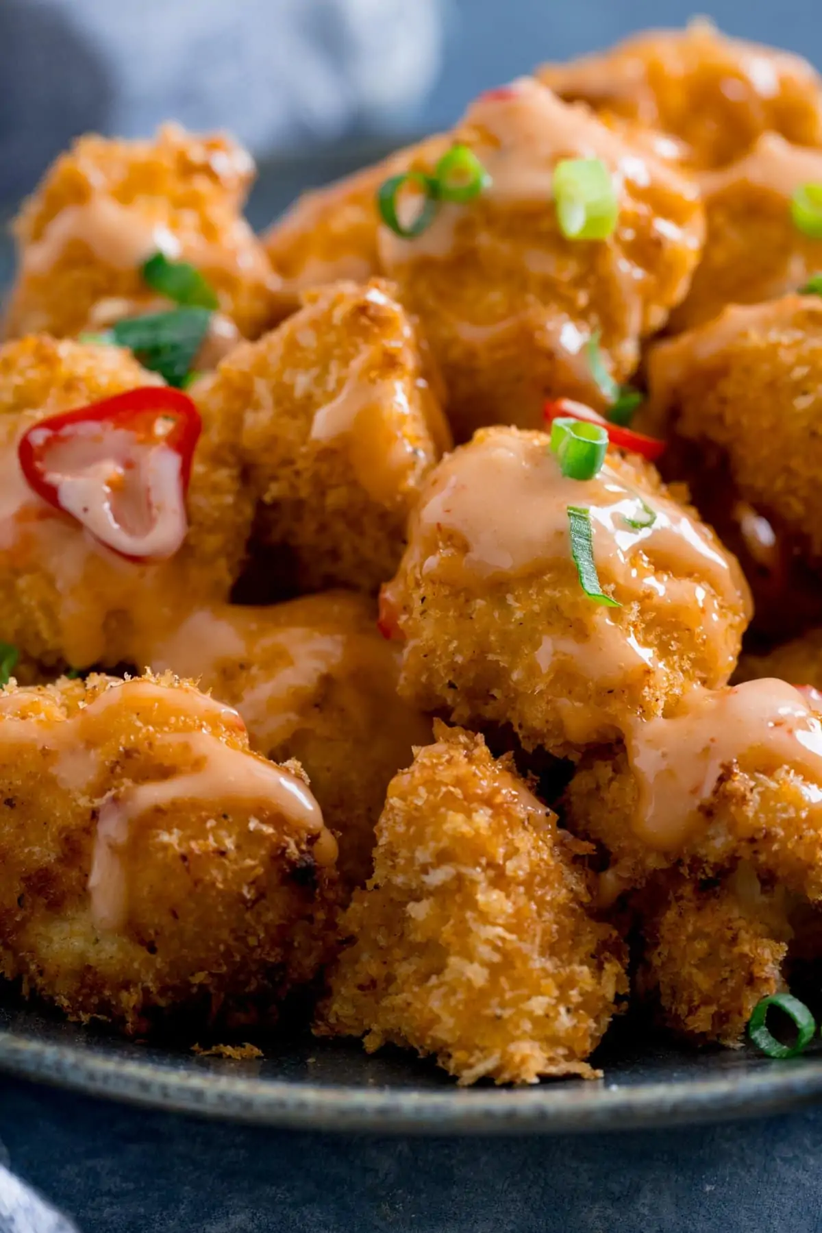 Bang bang cauliflower with chillies and spring onions on a dark plate.