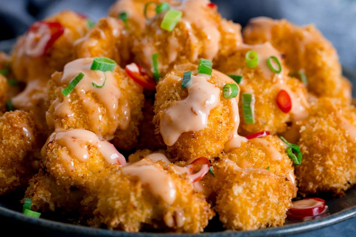 Crispy cauliflower florets piled on a plate, drizzled with a pink spicy sauce.