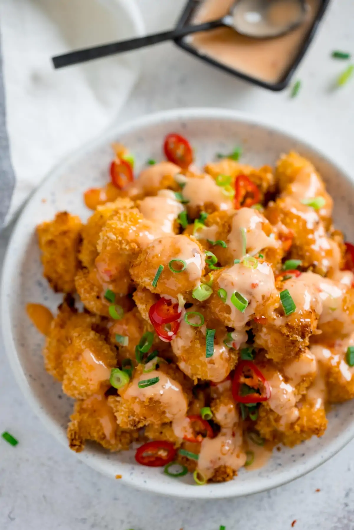 White bowl filled with bang bang chicken on a white surface.