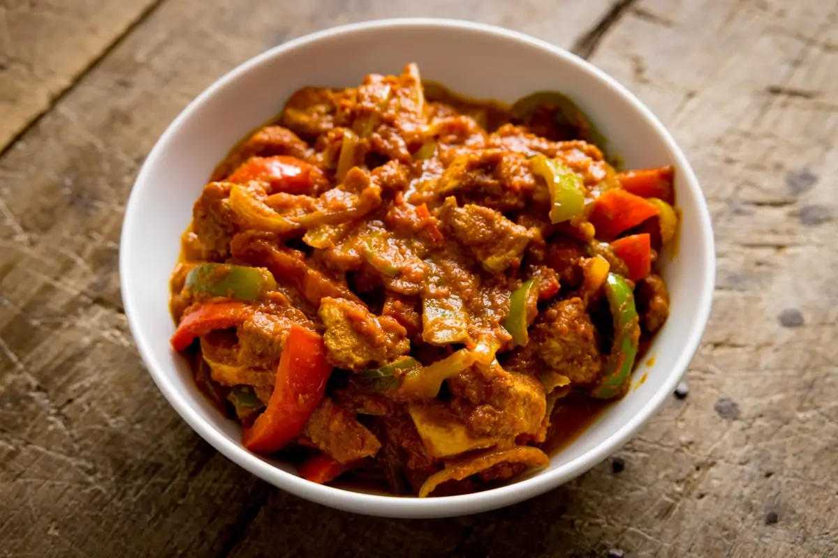 White bowl filled with chicken jalfrezi on a wooden table.