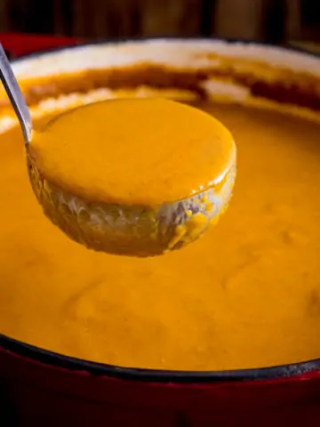 Ladle being lifted from a red cast iron pan containing curry base gravy.