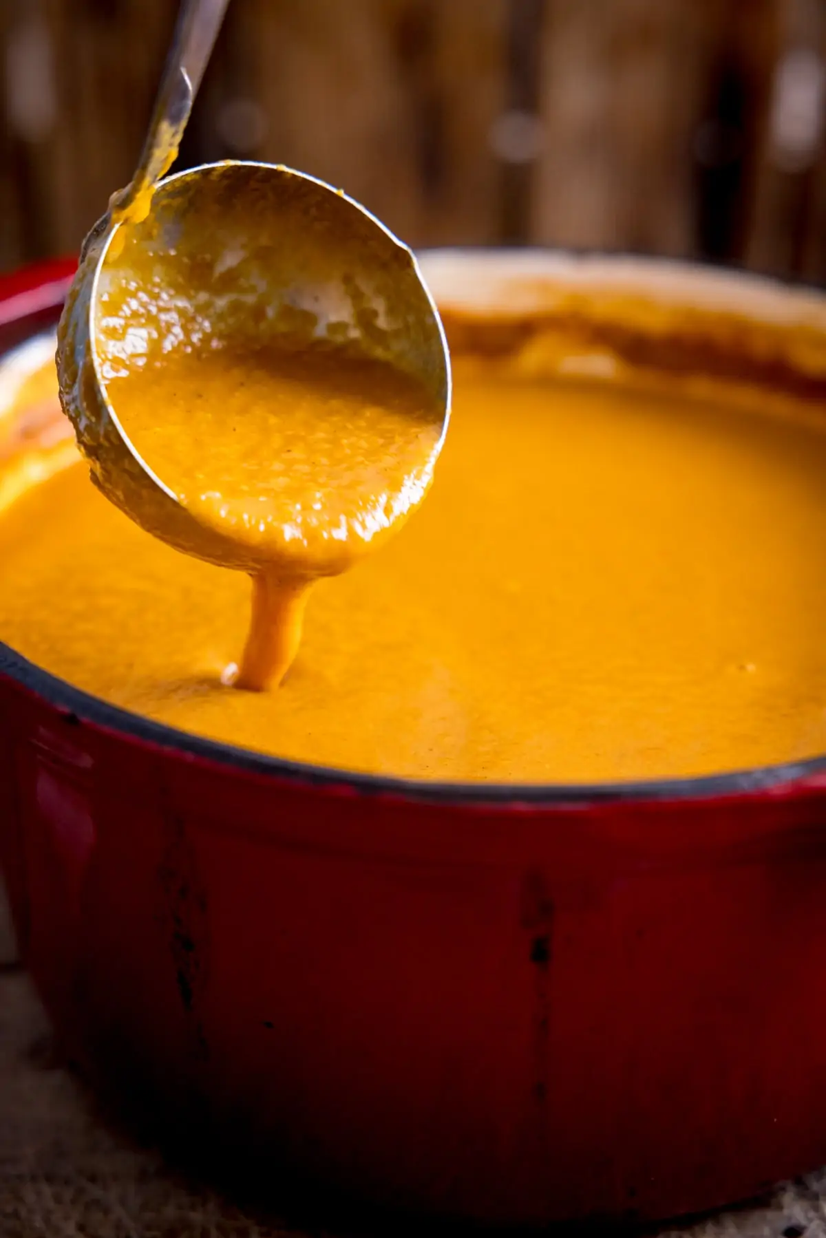 Ladle of curry base gravy being poured into a red cast iron pan.