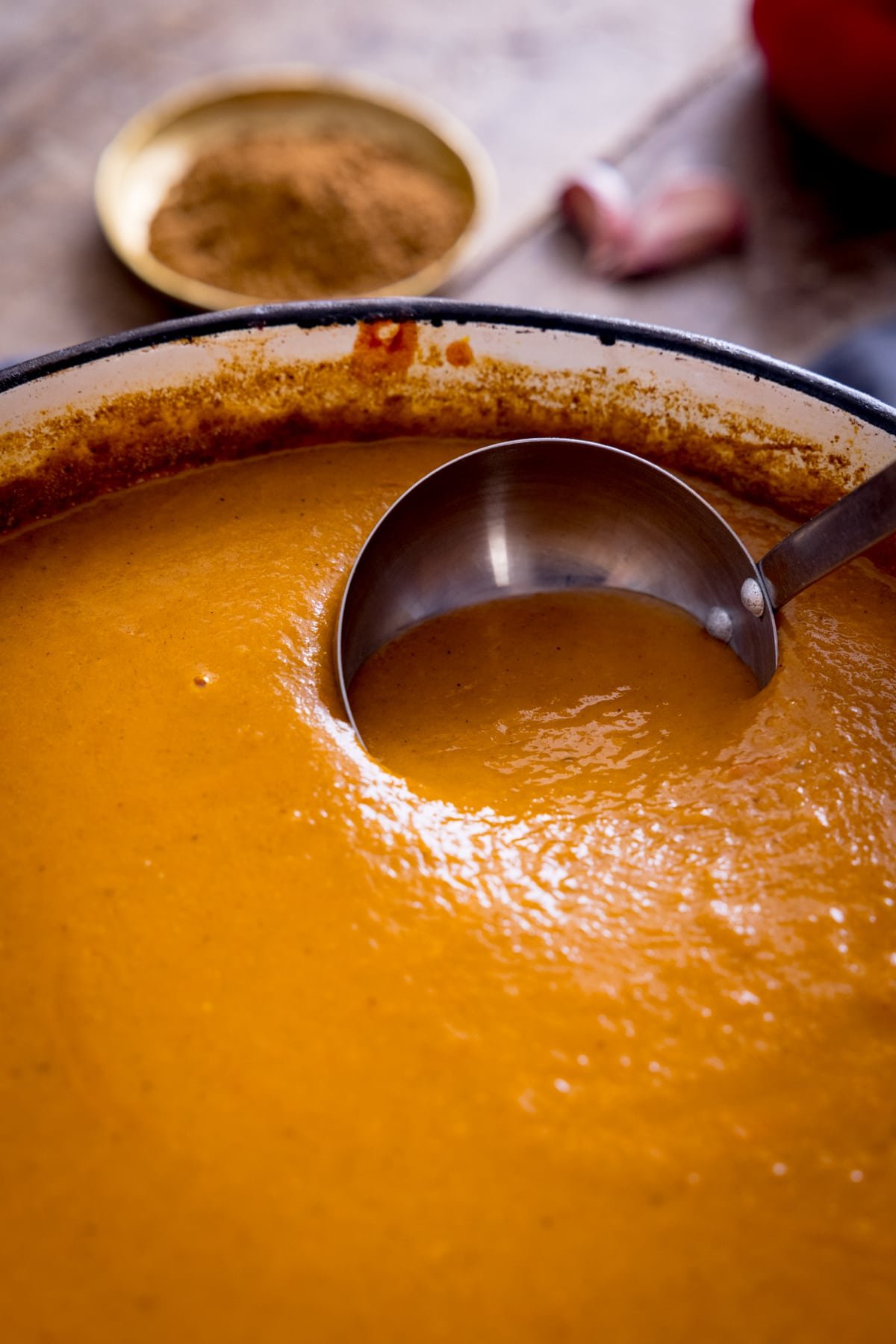 Ladle being dipped into a red cast iron pan filled with curry base gravy.