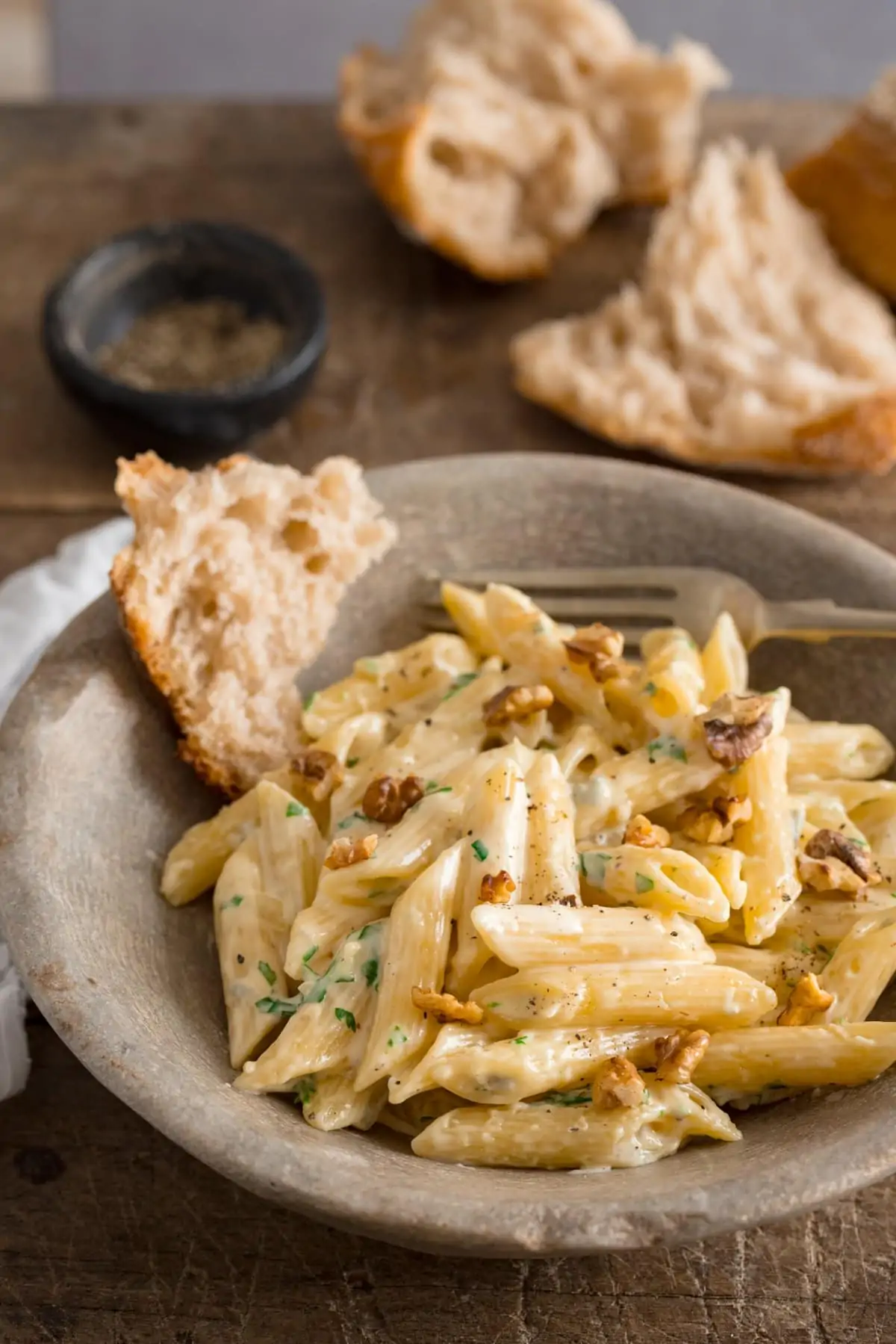 Gorgonzola pasta in a stone bowl on a wooden table. Pieces of bread in the bowl and in the background.