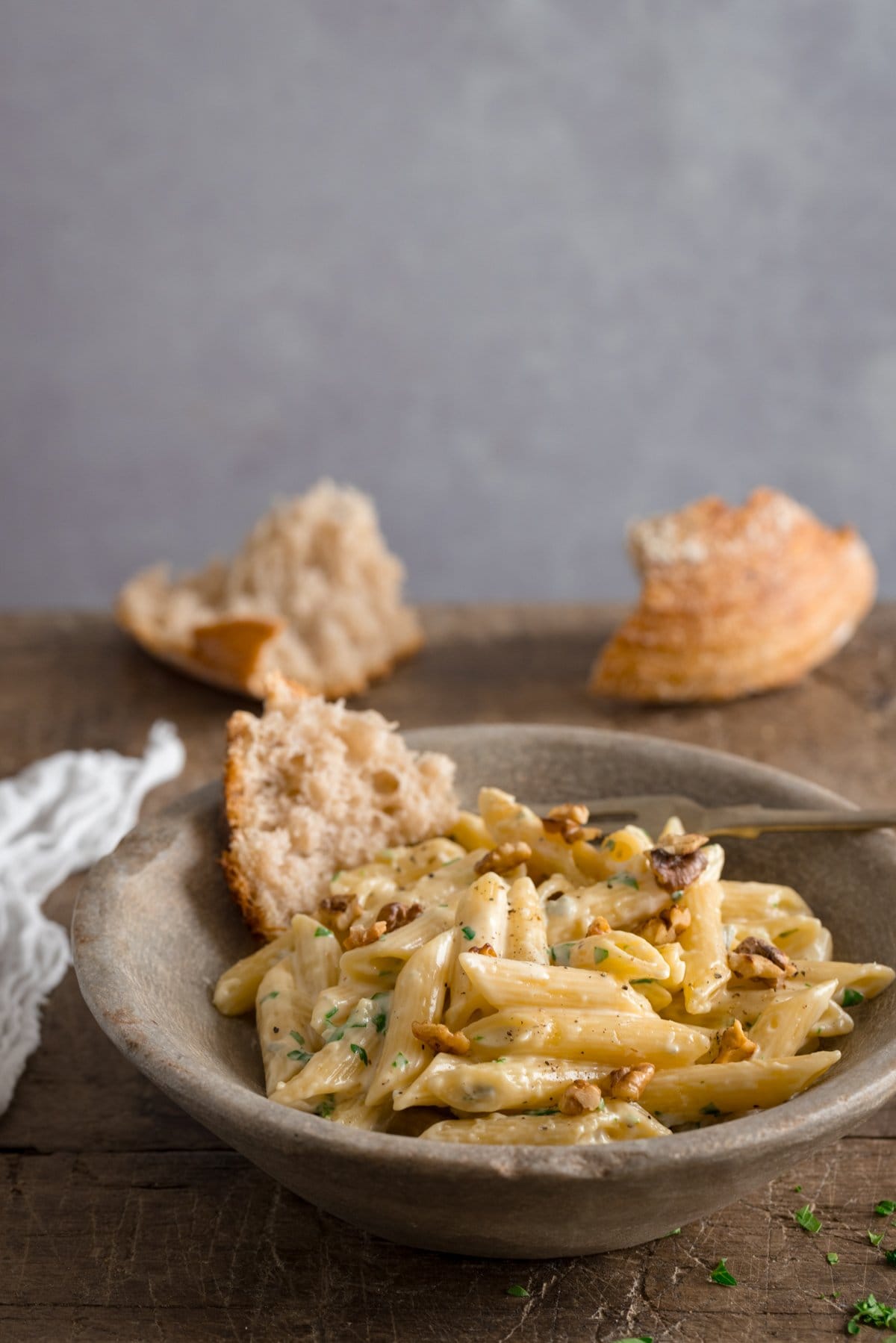 Stone bowl filled with gorgonzola penne pasta on a wooden table against a light grey background.