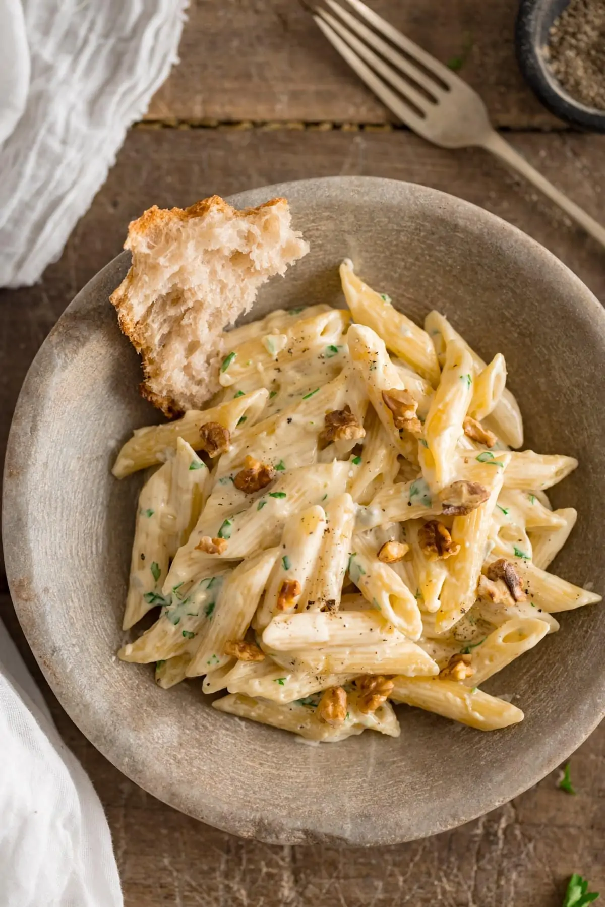 Overhead image of gorgonzola pasta in a stone bowl on a wooden table. There is a chunk of bread in the bowl with the pasta.