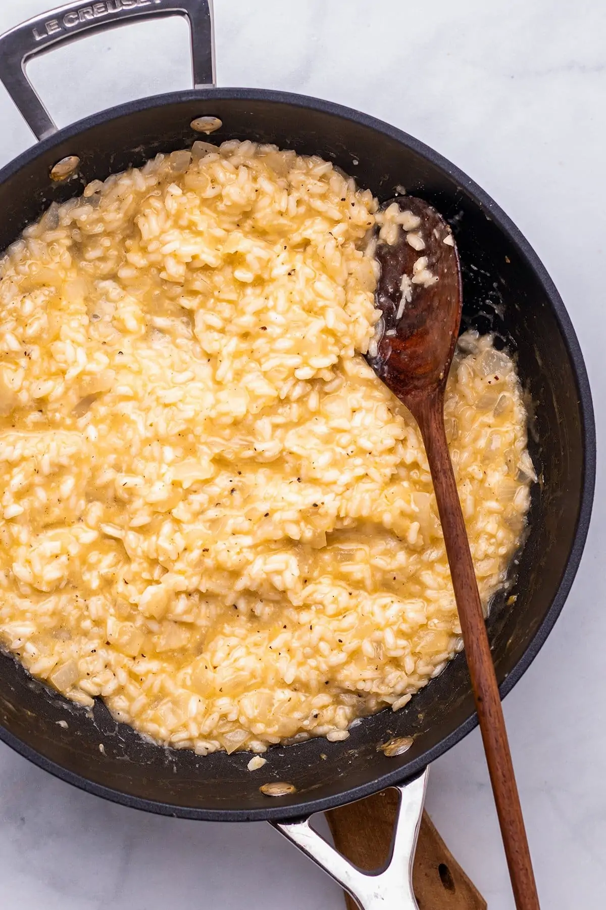Overhead photo of lemon risotto in a pan with a wooden spoon sticking out of it.