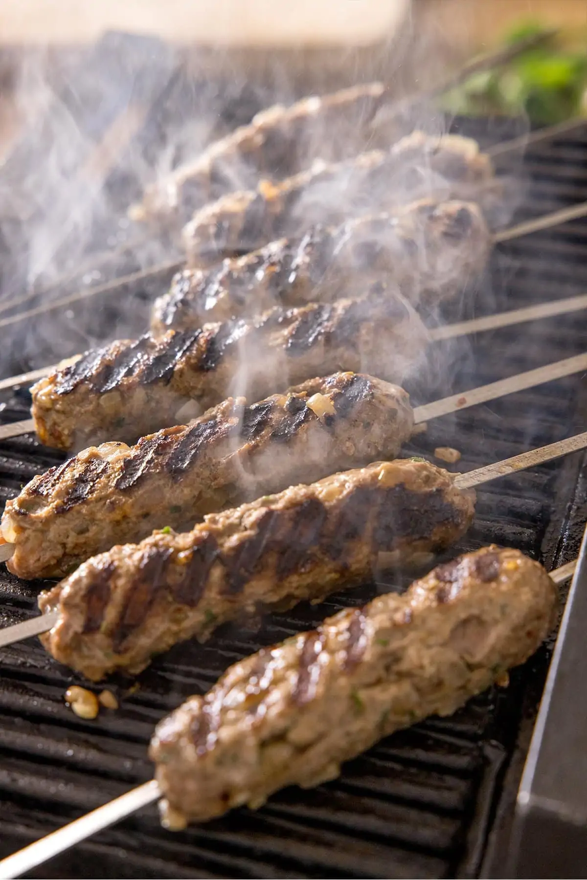 Lamb koftas being cooked on a griddle with steam rising.