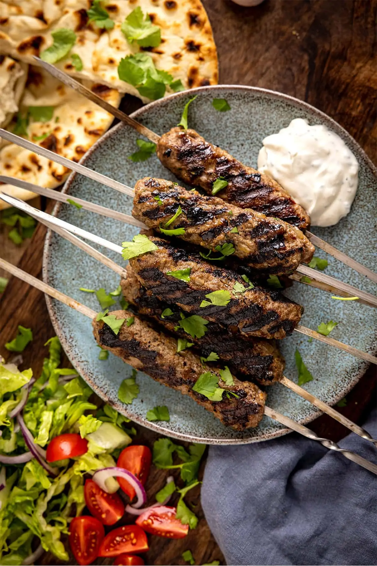 Overhead picture of Lamb Kofta Kebabs pilled up on a plate with some flatbreads and salad in the background.