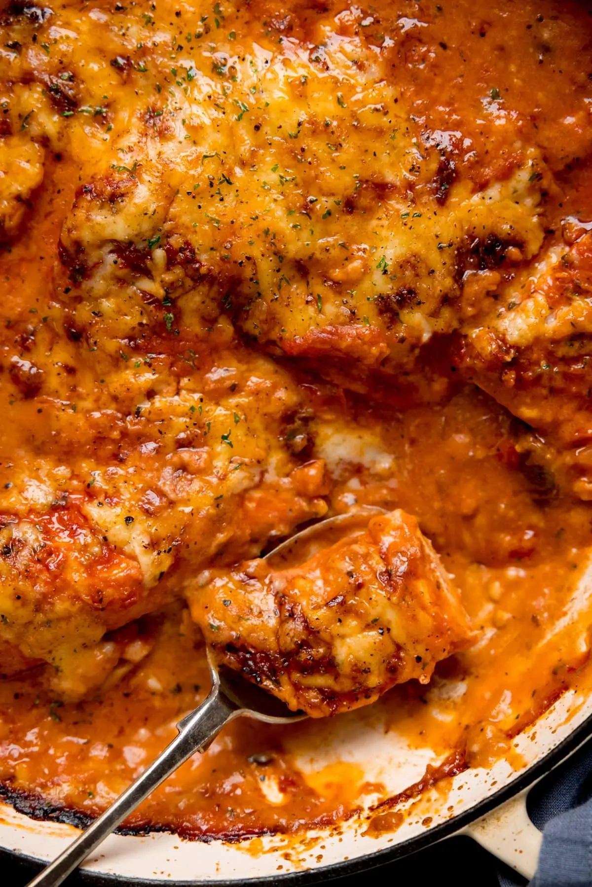 Close up of a spoonful of chicken being taken from a pan of lasagne-style chicken bake.