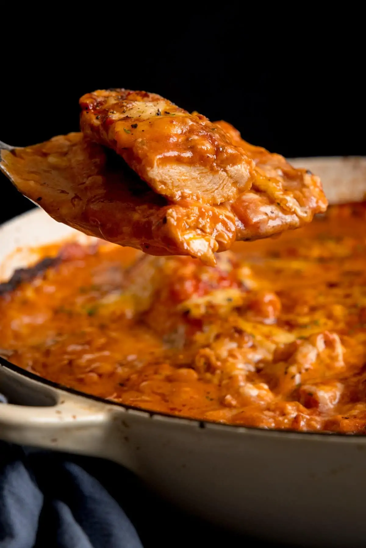 Side image of a spoonful of chicken being lifted from a pan of chicken tomato bake.