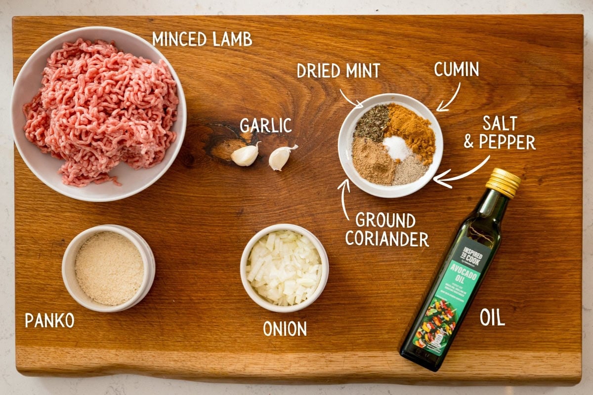 lamb kofta ingredients A wooden board displays the key ingredients for a Lamb Kofta Recipe: minced lamb, panko breadcrumbs, chopped onion, garlic cloves, spices such as dried mint and cumin, salt and pepper, plus a bottle of oil—perfect for preparing delicious lamb kofta.