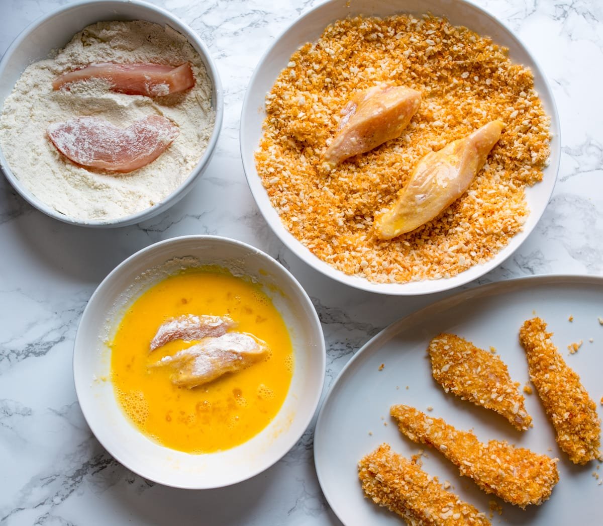 Strips of chicken being dipped into flour, then eggs then into a panko breadcrumb mixture.